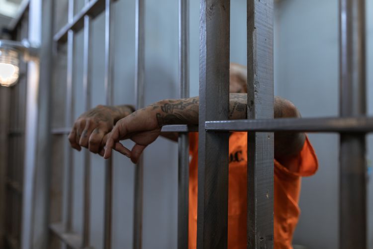 Prisoner in orange jumpsuit behind bars