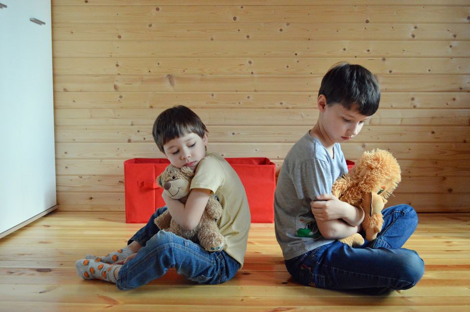 Sibling children sitting hold their teddybears looking sorry. 